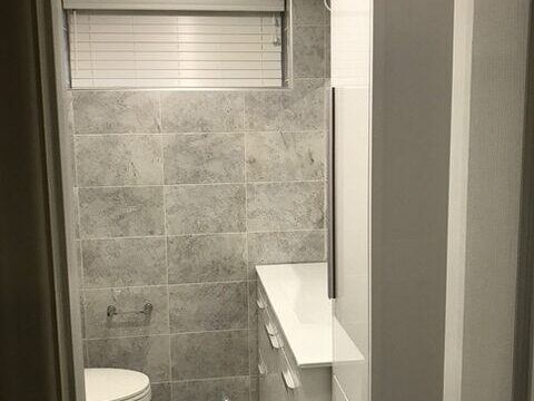 Bathroom renovation by David's Quality Renovations, featuring a tiled floor and walls, with white furniture visible (toilet, vanity and drawers).